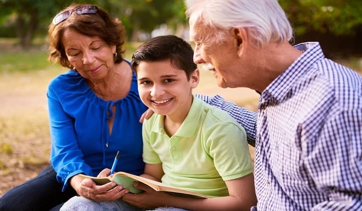 Grandparents educating grandson: Senior woman and old man spending time with their grandchild in park. The old people help the preteen boy doing his school homework. The kid looks at camera